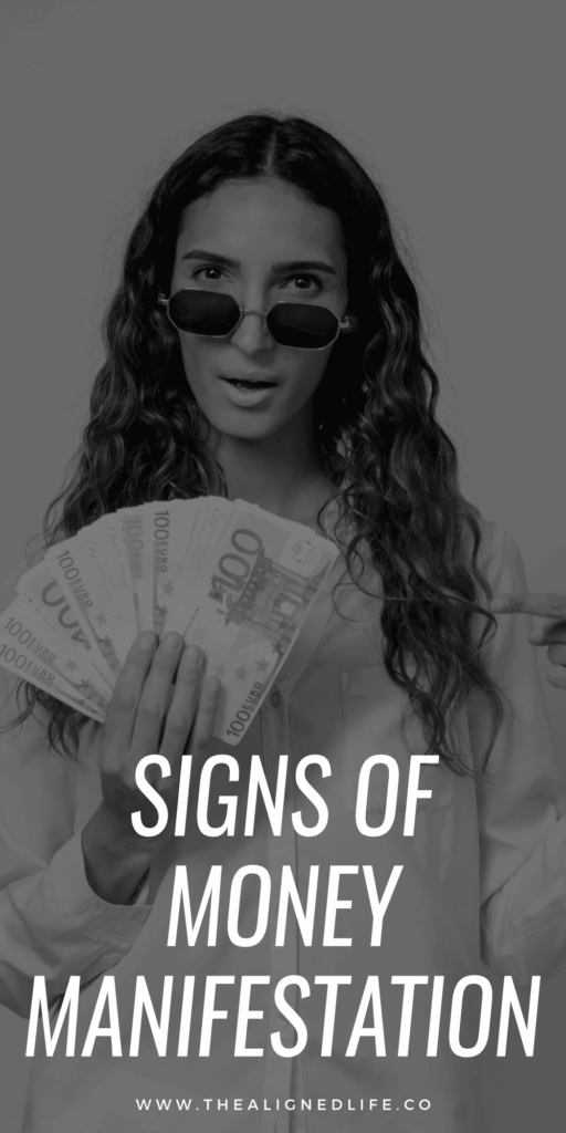 woman holding a handful of cash in front of a pink wall | Signs That Money Is Coming Your Way | The Aligned Life Manifestation Blog