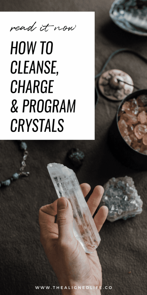 hand over a dark wood table holding a crystal | How To Cleanse, Charge & Program Crystals | The Aligned Life Manifestation Blog