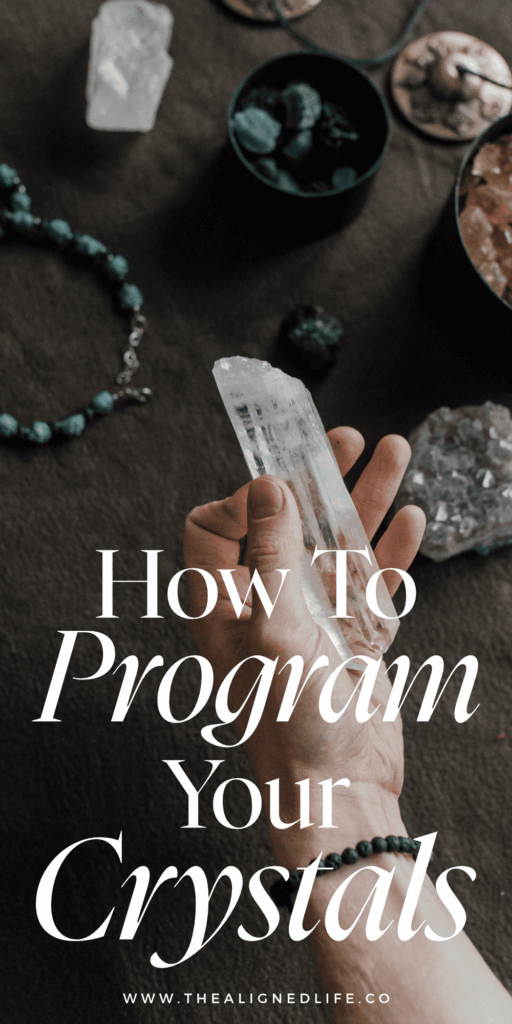 hand over a dark wood table holding a crystal | How To Cleanse, Charge & Program Crystals | The Aligned Life Manifestation Blog
