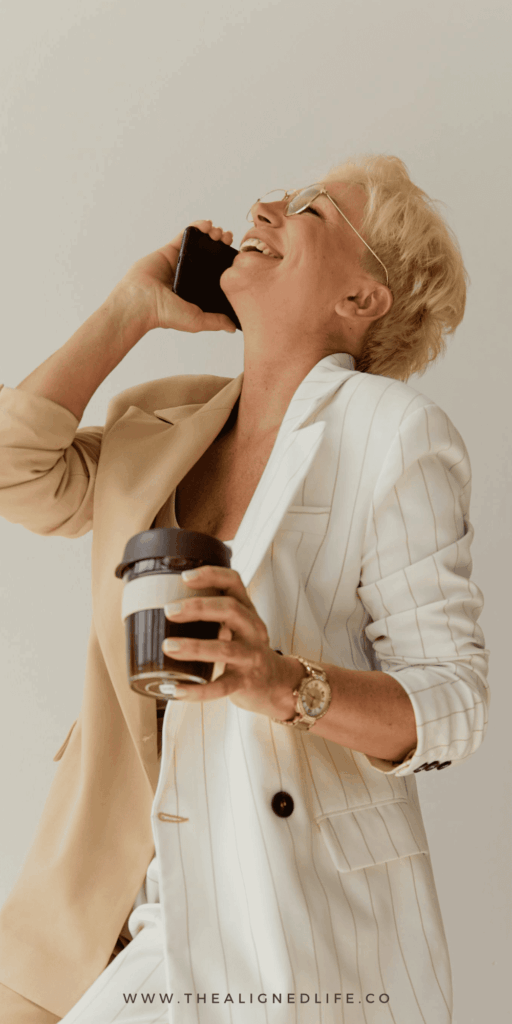 blonde woman in a beige jacket laughing on a cellphone | How To Manifest Your Dream Job | The Aligned Life Manifestation Blog