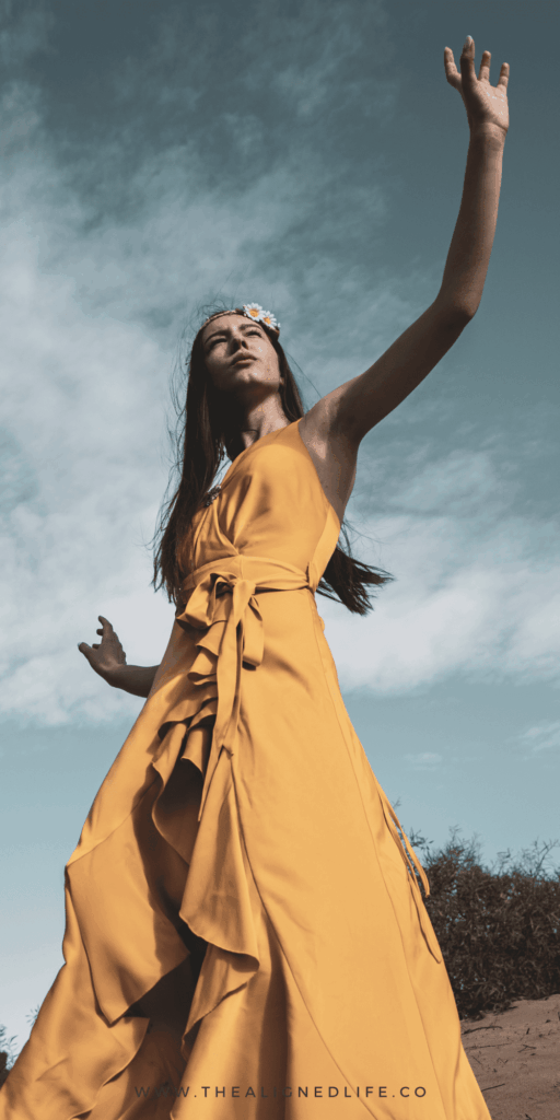 woman in a yellow dress with her hand against the sky | How To Use The 21 Universal Laws | The Aligned Life Manifestation Blog